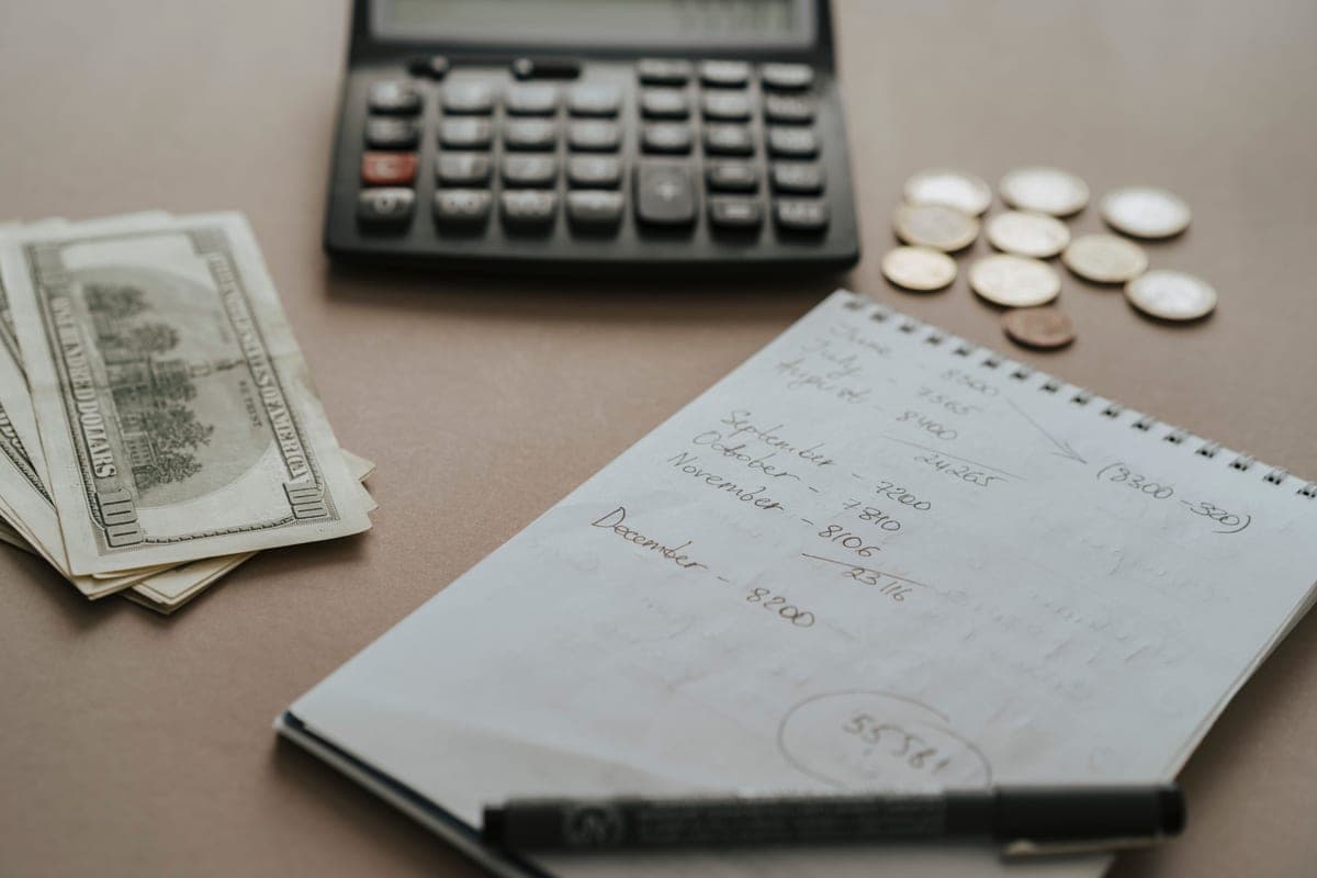 A desk with a calculator, cash, coins and handwritten notes