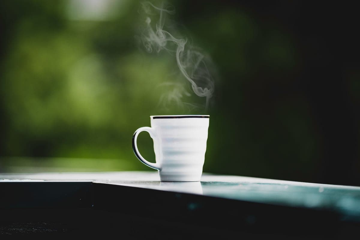 A steaming cup of coffee on a table with a blurred green background
