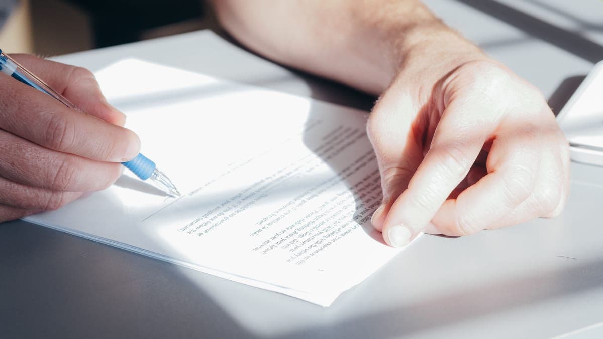 Hands signing a document with a blue pen, close up