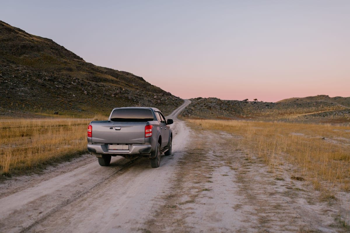 A pickup truck driving down a dusty dirt road at sunset