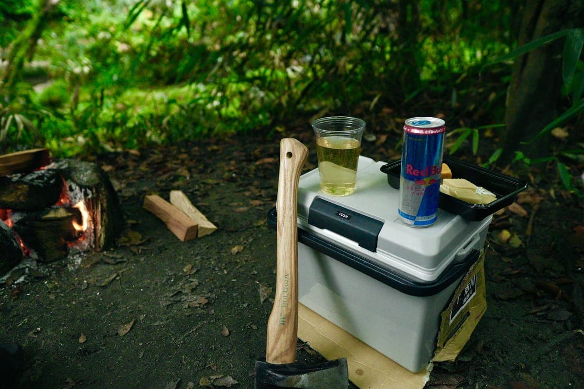 Illustrative stock photo: a campsite with a hard cooler, an axe and a small fire