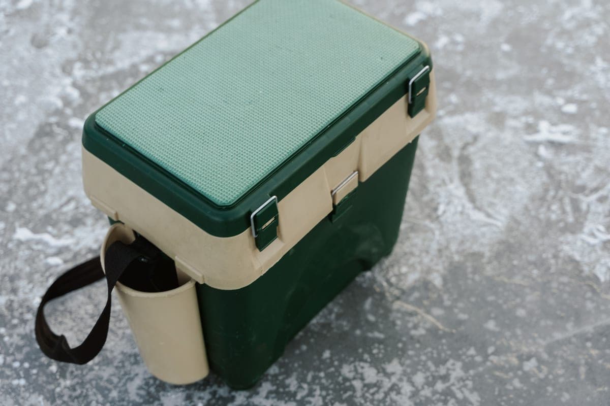 Illustrative stock photo: a green and beige hard cooler sitting on a frozen lake surface