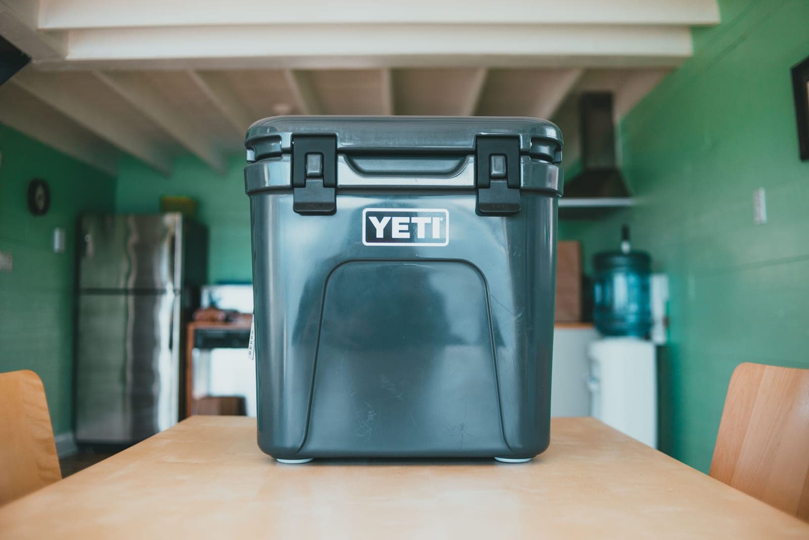 A dark gray rotomolded hard cooler with two rubber latches sitting on a wooden table